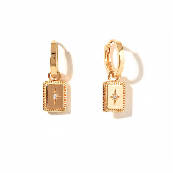 Charm Star Tag Huggies, Evocative of captivating talisman-inspired motifs, these gold hoop earrings are enhanced by an alluring charm centered with a dazzling cubic zirconia stone.  Materials: Eco Brass 5A Cubic Zirconia 18K Gold Plating